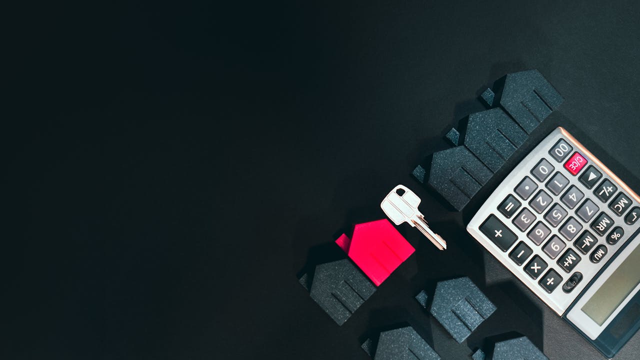 Real estate concept image featuring a calculator, houses, and a key on a black background.