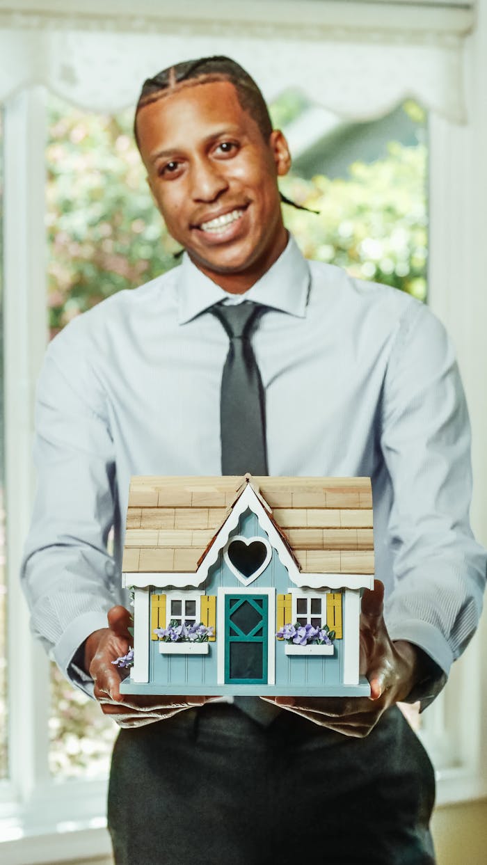 Smiling agent presents a charming miniature house, symbolizing real estate opportunities.